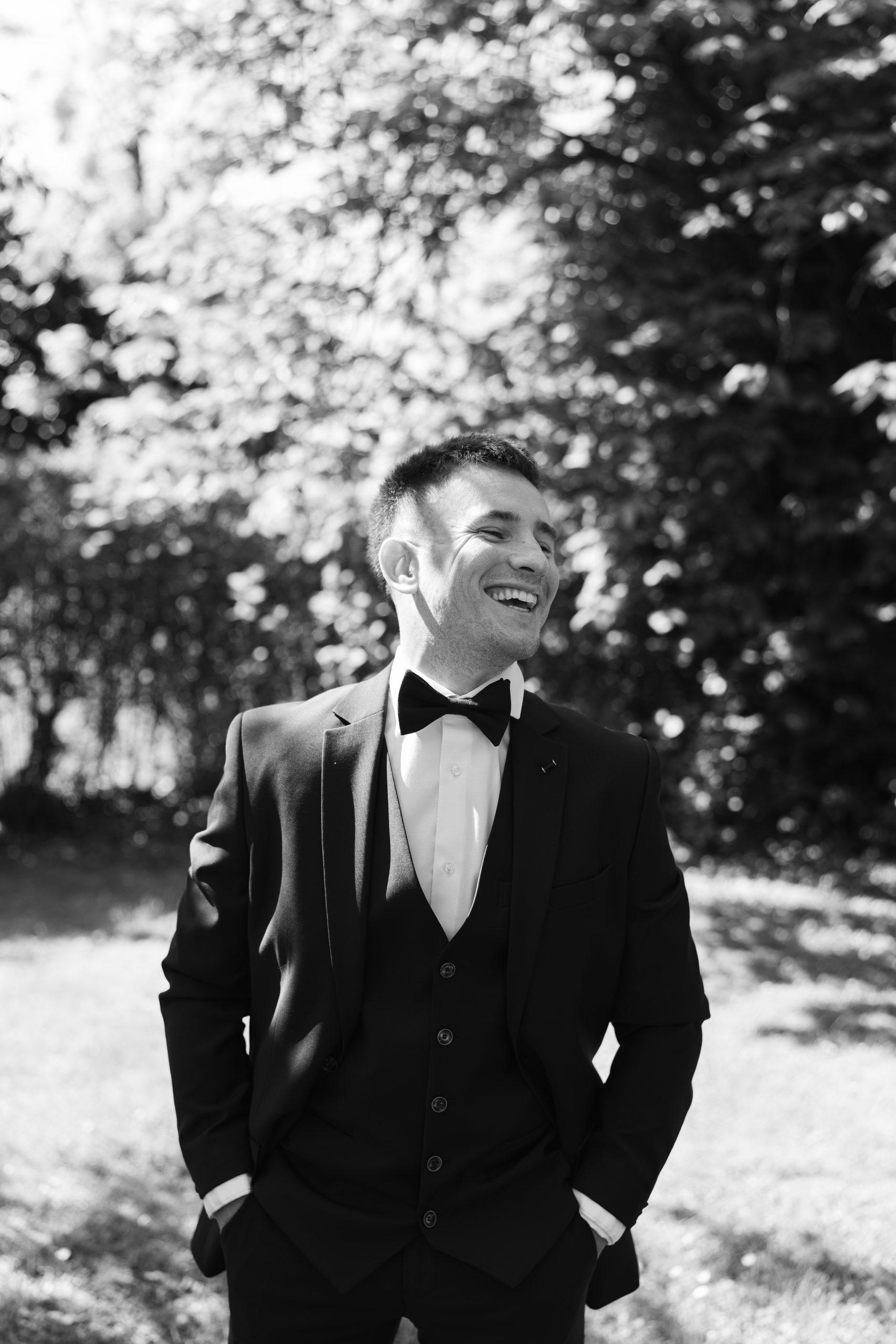 Portrait en noir et blanc de Théo souriant en costume de mariage dans un jardin